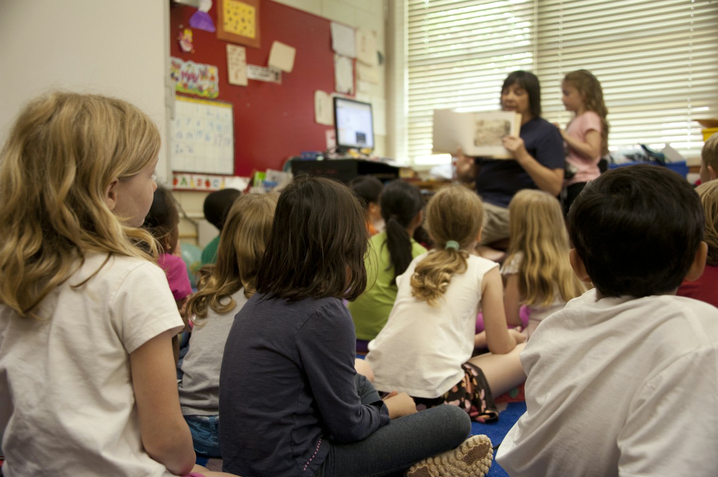 Lehrerin liest jungen Kindern vor, die auf einem gemusterten Teppich sitzen.