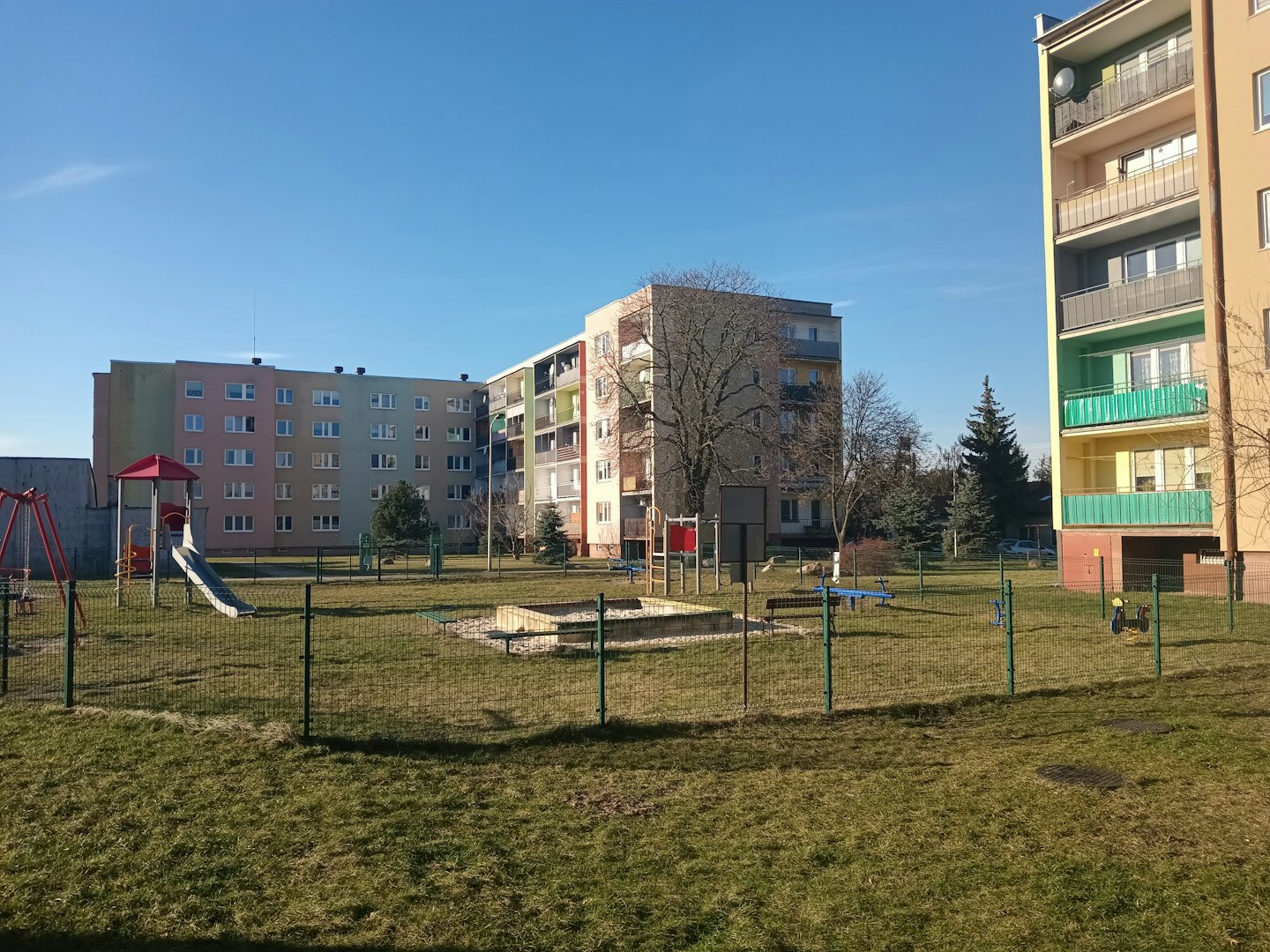 Spielplatz mit Schaukeln und Rutsche auf einer Rasenfläche.