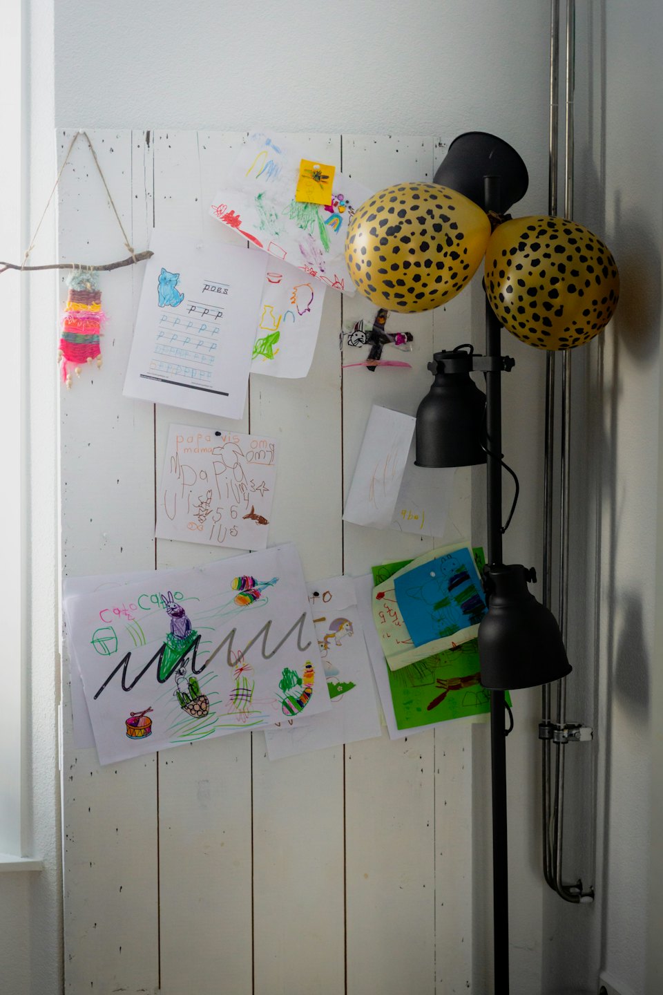 Kinderzeichnungen an einer weißen Holzwand mit Ballons und einer Lampe.